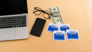 Laptop, smartphone, glasses, and Clareex wipes arranged neatly on a wooden table, representing tech care and resale value protection