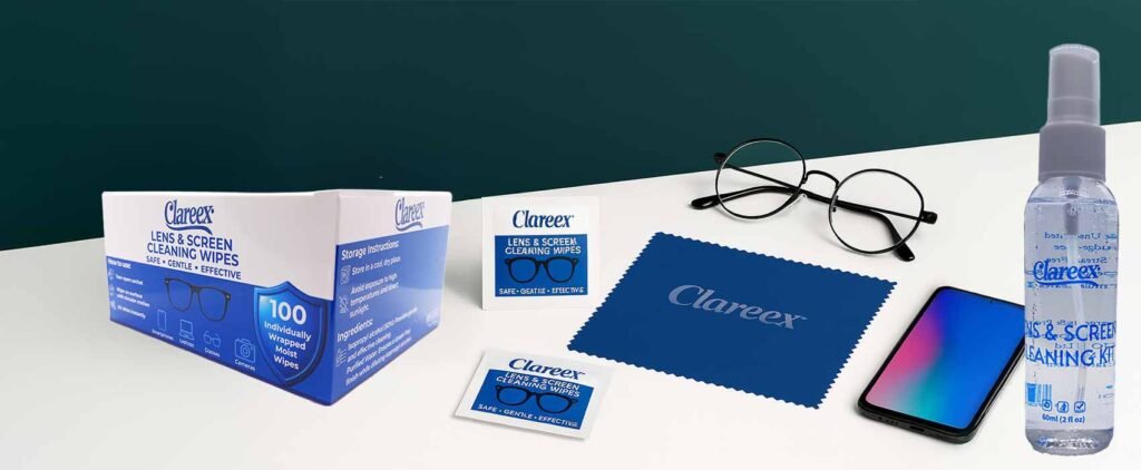 A high-resolution photograph displaying the Clareex lens and screen cleaning kit, including two individually wrapped wipes, a folded blue microfiber cloth, black round eyeglasses, and a smartphone, all arranged on a clean white surface.